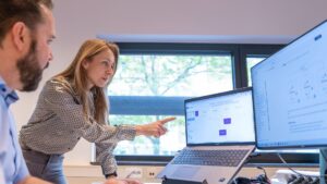 Medewerker wijst iets aan op beeldscherm terwijl andere medewerker toekijkt