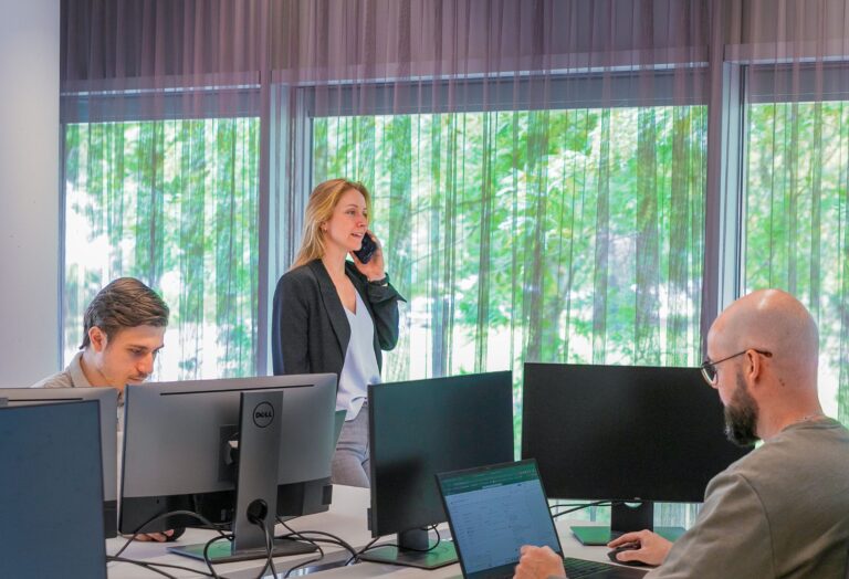 Een medewerker aan het bellen terwijl twee andere medewerkers bezig zijn achter hun computer
